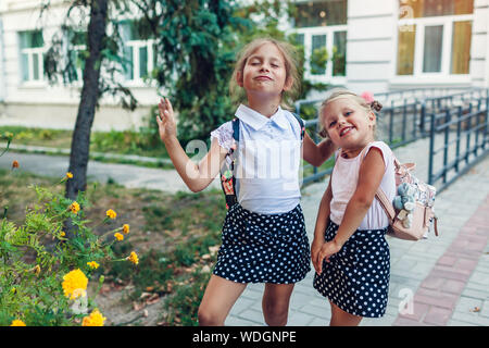 Zwei Schwestern Schüler mit Rucksäcken Grimasse im Freien Grundschule nach Klassen. Kleine Mädchen, die Spaß haben. Happy kids Lächeln Stockfoto