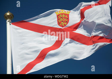 Die die Flagge der Mitgliedstaaten von Jersey in den Wind vor blauem Himmel. Die Vogtei Jersey ist die größte der Kanalinseln. Britische Inseln. Stockfoto