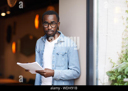 Portrait der Afrikanischen jungen Mann in Brillen und legere Kleidung, Dokumente und Kamera Stockfoto