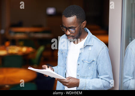 Junge afrikanische Menschen tragen Brillen ausfüllen, um die Dokumente in die Hände, während in der Nähe der Eingang im Restaurant stehen Stockfoto