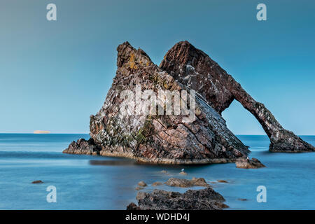 Bogen GEIGE ROCK PORTKNOCKIE Moray in Schottland abends LICHT AUF DEN FELSEN, UND DIE LICHTER VON EINEM KREUZFAHRTSCHIFF AM HORIZONT Stockfoto