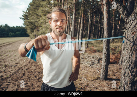 Junger Mann mit einem Widerstand Band, die in der Natur zu arbeiten Stockfoto