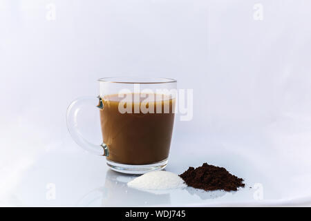 Eine frische Tasse Kaffee in einem Glas mug. Es gibt s kleiner Haufen von Zucker und Kaffee vor Stockfoto