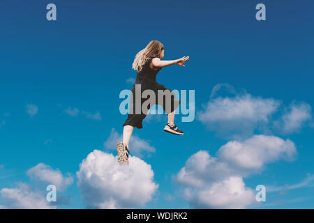 Süße Mädchen springen Lustig in Wolken über der Erde. Happy kleines fröhliches Mädchen zu Fuß durch. Levitation Konzept Stockfoto