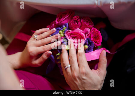 Sie haben verlobungsringe an ihren Händen. Sie legen ihre Hände auf Rosa und Lila gel Blumensträuße. Stockfoto