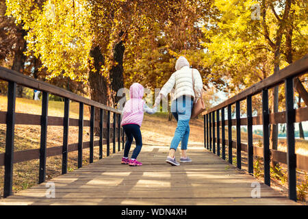 Mutter und wenig Vorschüler Tochter Spaß und Aprilscherze im Herbst City Park. Mutter und Kind laufen und springen auf rustikalen Holzbrücke in Stockfoto