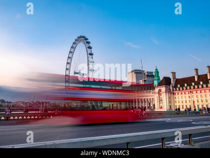 Fotos mit langer Belichtungszeit von Double Decker roter Bus in Bewegung auf die Westminster Abbey Brücke gegen das Auge von London in England Stockfoto