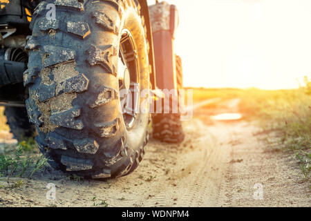 Close-up Schwanz Blick auf ATV Quad Bike auf Schmutz Land straße bei Sonnenuntergang am Abend Zeit. Dirty Rad der AWD All-terrain vehicle. Reisen und Abenteuer Konzept Stockfoto