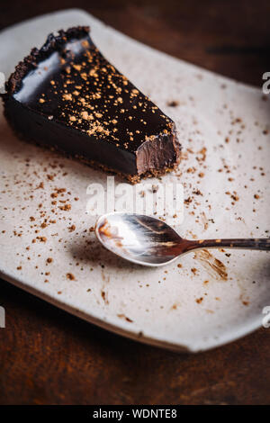 Scheibe der Raw vegan reichen dunklen Schokolade Kuchen auf einem weißen Teller im Restaurant. Nahaufnahme, Minimalismus Essen photograohy Konzept Stockfoto