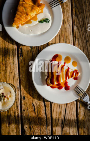 Zwei Scheiben Herbst Kürbis Kuchen mit Sahne und Marmelade Soße auf rustikalen Holztisch von oben. Essen Fotografie Konzept. Direkte Sonneneinstrahlung Stockfoto