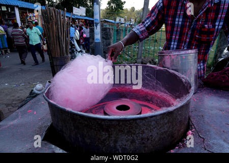 Ein junger Mann mit einem Bart von einem kaukasischen Trader in den Hut der Eigentümer der Steckdose macht Zuckerwatte, fairy Glasschlacke oder Zuckerwatte im Sommer Park. Stockfoto