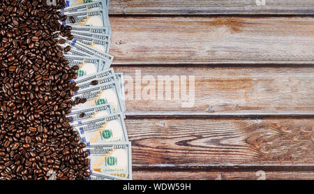 Banknote von 100 US-Dollar, zwischen der Kaffeebohnen der Verkauf, die Lieferung und Verteilung von Kaffee auf Holz- Hintergrund Stockfoto