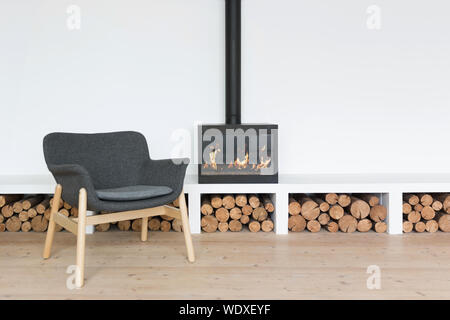 Gemütliche minimalistischen Interieur mit Kamin in einem hellen Raum mit einem Woodpile und einem Sessel Stockfoto