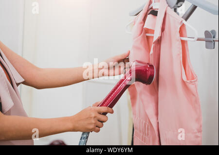 Frau mit Dampf Bügeleisen Bügeln Fashion Shirt in der Waschküche. Mädchen tun stream Dampf Bügeleisen für Presse Kleidung in der Hand. Waschen konzentrieren, um eine Stockfoto