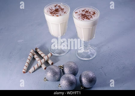 Zwei selbstgemachte Eierlikör Milchshakes mit Zimt, Weihnachten Dekorationen auf einem blauen Hintergrund. Weihnachtliche Atmosphäre. Stockfoto