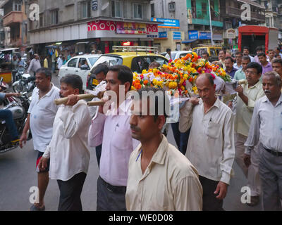 Verwandten eines Verstorbenen Hindu tragen die mit Blumen geschmückte Körper auf einem gurney für die letzte Ölung in einem nahe gelegenen Krematorium; Chira Bazar, Mumbai, Indien Stockfoto