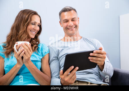 Portrait von lächelnden Reifes Paar sitzt auf einem Sofa Video In digitaler Tablette zu Hause Stockfoto