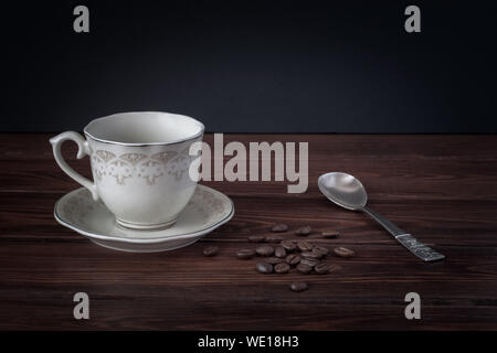 Leere Kaffeetasse auf eine Untertasse, Kaffeebohnen auf dunklen Tabelle Boards. Schönen silbernen Löffel. Für Text platzieren. Stockfoto