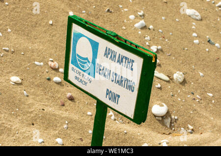 Schild mit dem Bild der Blauen Fahne und der Aufschrift "Strand Ausgangspunkt' im Hintergrund von Sand und weiße Steine Stockfoto