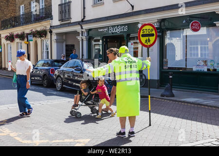 England, Berkshire, Eton, Eton High Street, Lollipop Lady Holding Stoppschild mit Fußgänger die Straße überqueren Stockfoto