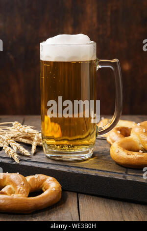 Ein mug Lagerbier mit deutschen Brezeln. Helles Bier auf einem dunklen Holztisch. Stockfoto