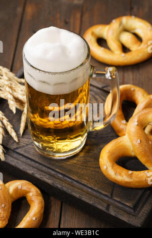 Ein mug Lagerbier mit deutschen Brezeln. Helles Bier auf einem dunklen Holztisch. Stockfoto