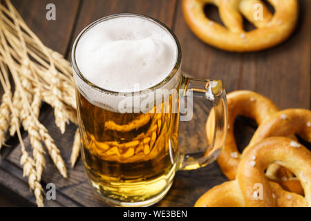 Ein mug Lagerbier mit deutschen Brezeln. Helles Bier auf einem dunklen Holztisch. Stockfoto