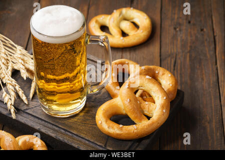 Ein mug Lagerbier mit deutschen Brezeln. Helles Bier auf einem dunklen Holztisch. Kopieren Sie Platz. Stockfoto