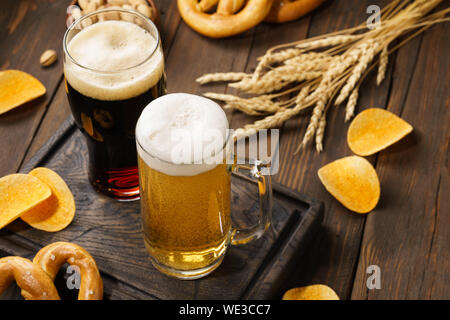 Helle und dunkle Bier mit verschiedenen Snacks - Chips, Brezeln und Muttern auf einem dunklen Hintergrund. Stockfoto