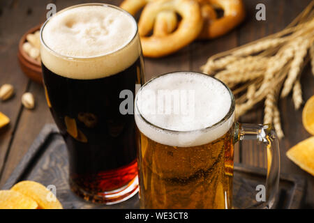 Zwei Gläser Bier - Licht und Dunkel mit verschiedenen Snacks im Hintergrund. Nahaufnahme. Stockfoto