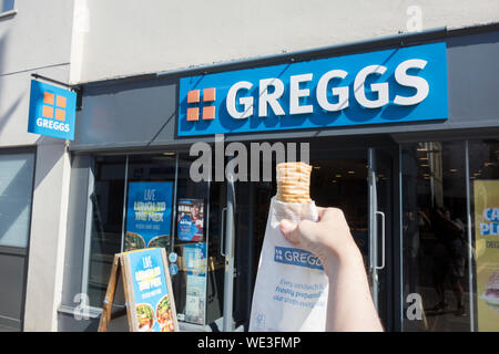 Eine junge Frau, die Hand mit einem Greggs vegan-freundlich Wurstbrötchen außerhalb einer Greggs in Richmond, Surrey, Großbritannien Stockfoto