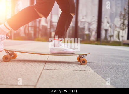 Bild der Frau in weißen Turnschuhen, Skateboard fahren auf der Straße in der Stadt im Sommer. Lensflare Effekt Stockfoto