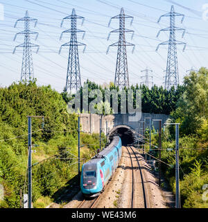 Ein doppeldecker TGV Duplex Hochgeschwindigkeitszug in Ouigo livery ist in einen Tunnel unter einer Reihe von Sendemasten auf der LGV Atlantique Eisenbahn. Stockfoto