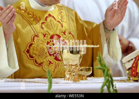 Kelch auf dem Altar und Priester feiern Gottesdienst im Hintergrund Stockfoto