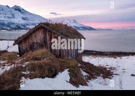 Arktische Landschaft in einem Fjord mit alten Hütte unter rosa Himmel bei Sonnenuntergang, Tromsö, Norwegen Stockfoto