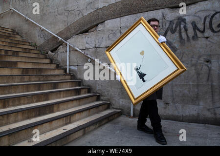 London, Großbritannien. 30 Aug, 2019. Der Christie Mitarbeiter wirft mit Kunstwerken" Mädchen mit Ballon - Farbe AP (Gold)" durch anonyme Street Artist Banksy an der Southbank Centre in London Freitag, 30. August 2019. Die Southbank Centre wurde in der Nähe einer der ursprünglichen Standorte die Kunstwerke in London erschien. Die Drucke werden auf Verkauf nur während einer Online Auktion mit dem Titel 'Banksy: Ich kann nicht glauben, dass sie Idioten dieser Sh*t" von Christie's Auktionshaus zwischen 11-24 September 2019 vorgestellt. Foto Credit: Lukas MacGregor/Alamy leben Nachrichten Stockfoto