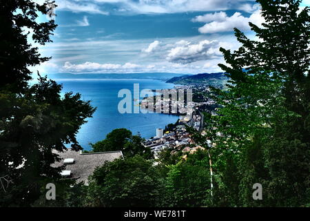 Hochwinkel-Panorama über Montreux und das Ufer des Genfer Sees, eingerahmt von üppigen grünen Bäumen unter einem dramatischen bewölkten Himmel, Waadt, Schweiz Stockfoto