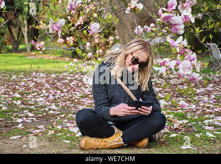 Porträt der jungen Frau im Park sitzen unter Magnolienbaum Stockfoto