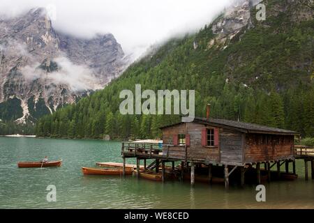 Italien, Autonome Provinz Bozen, Hochpustertal Tal, See von Prags, Frau Rudern in einem Boot vor ein Holzhaus auf Stelzen über den smaragdgrünen Gewässern der See durch die grünen Berge im Nebel gefangen umgeben Stockfoto