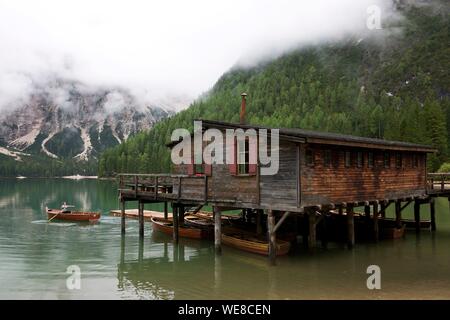 Italien, Autonome Provinz Bozen, Hochpustertal Tal, See von Prags, Frau Rudern in einem Boot vor ein Holzhaus auf Stelzen über den smaragdgrünen Gewässern der See durch die grünen Berge im Nebel gefangen umgeben Stockfoto