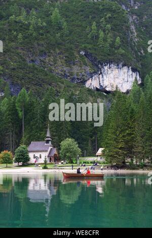 Italien, Autonome Provinz Bozen, Hochpustertal, See Pragser Tal, Ruderer in einem Boot auf dem smaragdgrünen Wasser des Sees mit einer Kirche auf der Bank und einem grünen Berg für die Dekoration Stockfoto