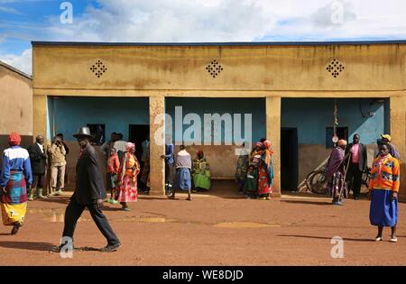 Ruanda, Zentrum des Landes, Dorfbewohner in farbenfrohe Outfits vor einem säulengang Gebäude in einem Dorf mit unbefestigten Straßen Stockfoto