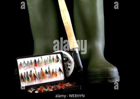 Fly Fishing Rod und Reel mit grünen waten Stiefel und Angeln fliegen in flybox auf schwarzem Hintergrund Stockfoto