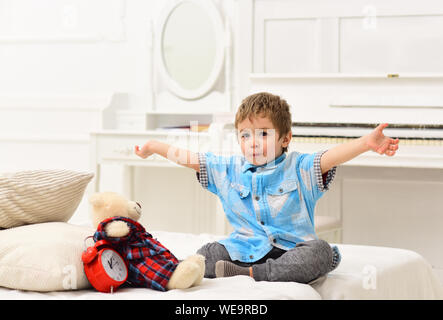 Kind im Schlafzimmer Märchen erzählen für Spielzeug. Märchen Konzept. Kid, Plüschbär in der Nähe von Kissen und Wecker, luxuriöse Innenausstattung Hintergrund. Junge mit f Stockfoto