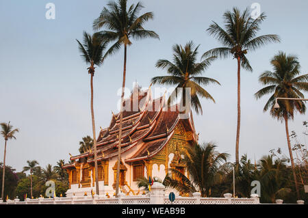 Luang Prabang, Laos - Luang Prabang Royal Palace Museum und Hor Prabang Temple Hall unter der Kokospalme mit schönen warmen Morgenlicht. Stockfoto