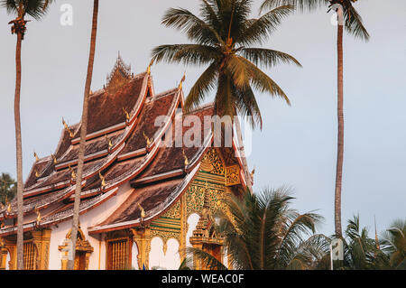 Luang Prabang, Laos - Luang Prabang Royal Palace Museum und Hor Prabang Temple Hall unter der Kokospalme mit schönen warmen Morgenlicht. Stockfoto