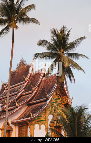 Luang Prabang, Laos - Luang Prabang Royal Palace Museum und Hor Prabang Temple Hall unter der Kokospalme mit schönen warmen Morgenlicht. Stockfoto