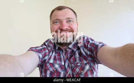 Selfie portrait! Gut aussehender bärtiger Mann unter selfie Foto und lächelnd auf dem hellen Hintergrund. Stockfoto