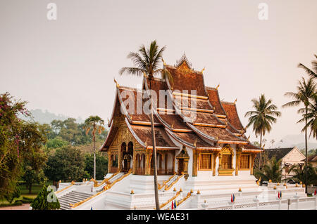 Luang Prabang, Laos - Luang Prabang Royal Palace Museum und Hor Prabang Temple Hall unter Coconut Tree mit schönen warmen Morgenlicht. Stockfoto