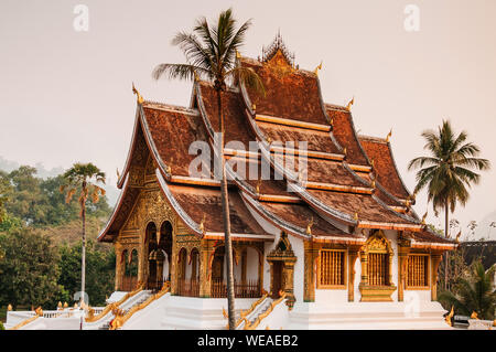 APR 4, 2018 Luang Prabang, Laos - Luang Prabang Royal Palace Museum und Hor Prabang Temple Hall unter Coconut Tree mit schönen warmen Morgenlicht. Stockfoto